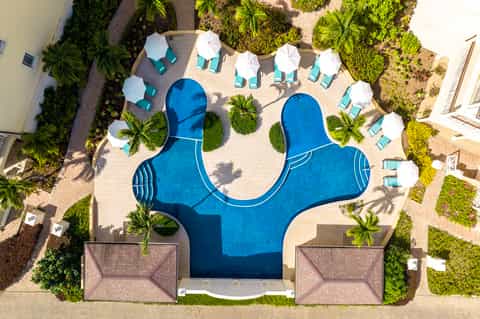 Aerial view of Mickey Mouse-shaped pool with white umbrellas, lounge chairs, and surrounding palm trees