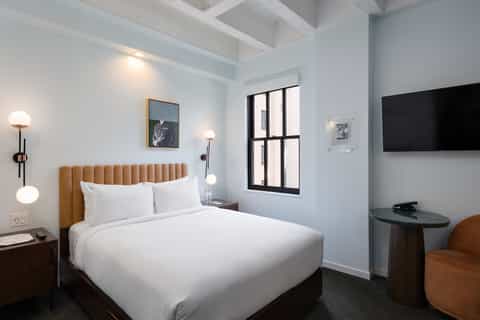 Modern hotel bedroom with tan headboard, white bedding, and minimalist décor