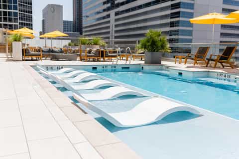 Urban rooftop pool with white lounge chairs, yellow umbrellas, and city skyline backdrop