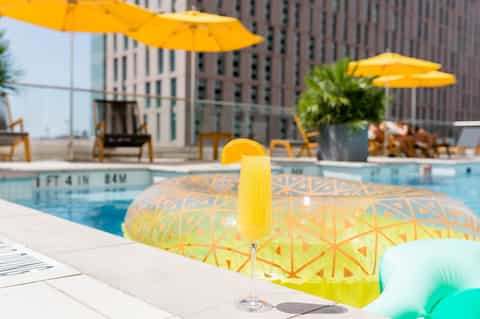 Rooftop pool bar with yellow umbrellas, cocktail, inflatable lounges, and downtown urban backdrop