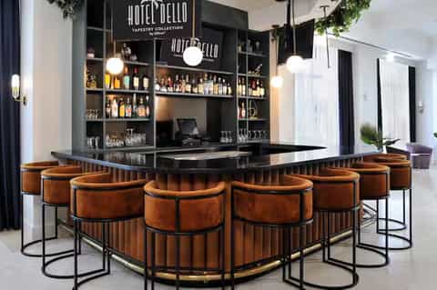 Modern hotel bar with copper barrel stools, black counter, and illuminated bottle display shelving