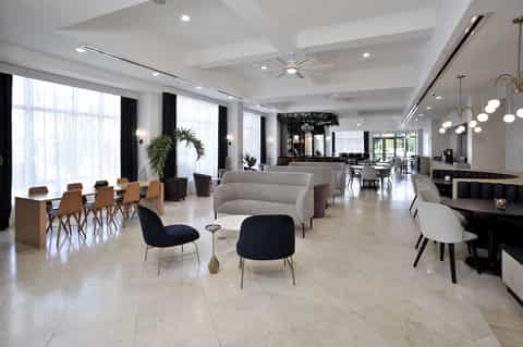 Spacious hotel lobby lounge with white ceiling, large windows, modern furniture, and natural lighting