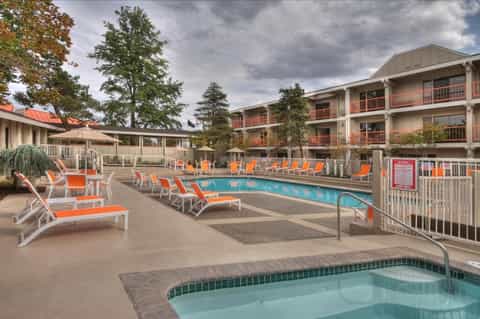 Resort pool deck with orange lounge chairs, multi-story building, and spa area with umbrellas