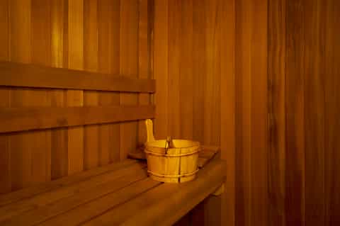 Wooden sauna interior with cedar walls, benches, and traditional wooden bucket for relaxation and wellness