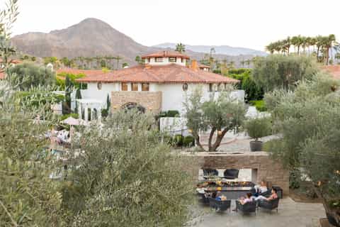 Spanish colonial-style villa with white walls, terracotta roof, and patio seating overlooking desert mountains