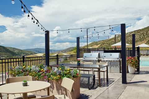 Resort rooftop terrace with mountain views, grill stations, string lights, outdoor furniture, and pool area