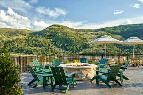 Mountain vista from resort deck with fire pit, green Adirondack chairs, white umbrellas, and forest landscape