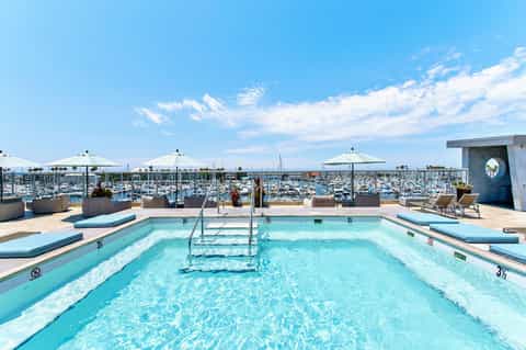 Rooftop swimming pool with marina views and white umbrellas on sunny day