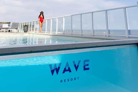 Indoor swimming pool with 'WAVE RESORT' text visible, ocean views beyond glass enclosure