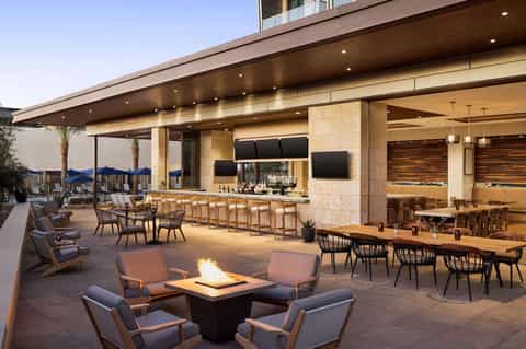 Outdoor terrace with fireplace, dining tables, bar, and lounge seating at dusk