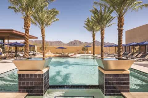 Luxury resort pool with palm trees, lounge chairs, and desert mountain backdrop