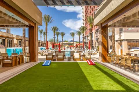 Indoor-outdoor space with green artificial turf, cornhole games, and pool view between buildings