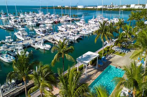 Aerial view of marina filled with white sailboats and yachts surrounded by turquoise water
