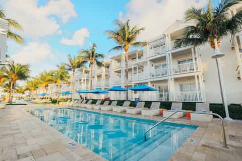 Residential resort pool with blue umbrellas, white buildings, and palm trees lining grounds