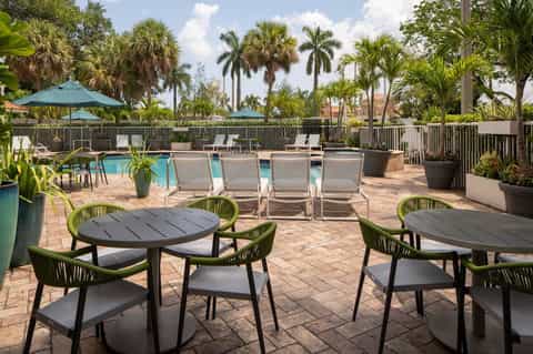 Tropical resort pool deck with lounge chairs, dining tables, umbrellas, and palm trees