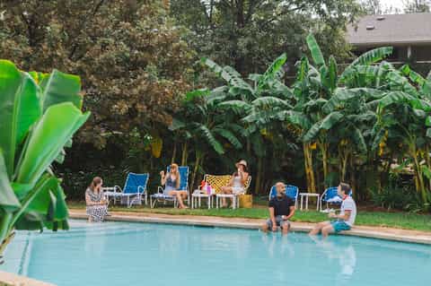 Resort pool with tropical landscaping, banana plants, and guests enjoying poolside lounge chairs