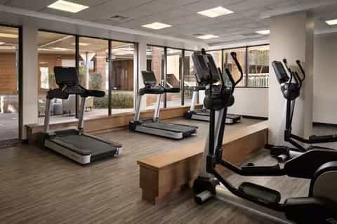 Fitness center with treadmills, elliptical machines, and large windows overlooking courtyard