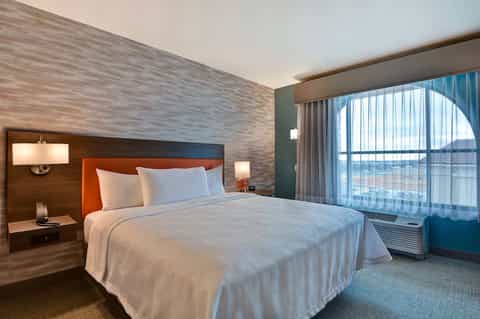 Upscale hotel bedroom with orange headboard, wood accent wall, ocean view, and contemporary furnishings