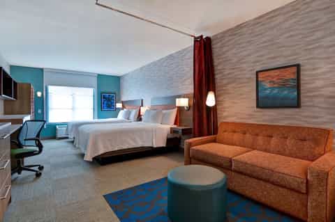 Contemporary hotel room with two beds, turquoise accent wall, and orange sofa