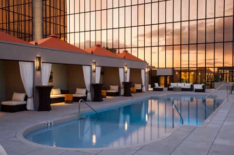 Contemporary rooftop pool with white cabanas, modern lighting, and floor-to-ceiling glass wall at dusk