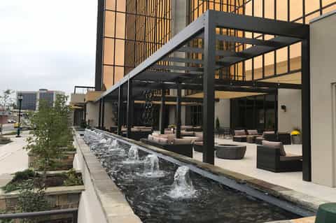 Contemporary outdoor patio with black pergola, lounge seating, water features, and tall buildings