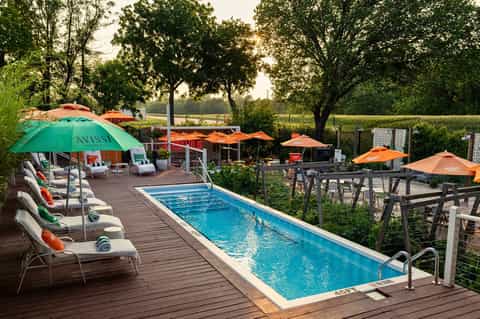 Lap pool with orange umbrellas, lounge chairs, and trees in rural resort setting