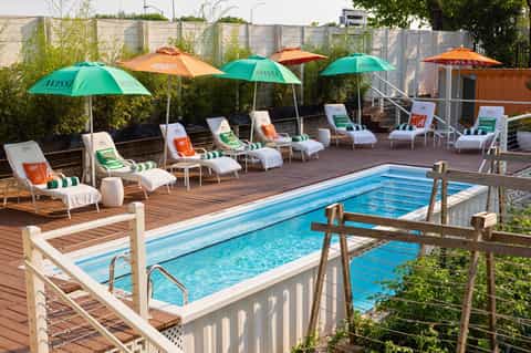 Resort pool deck with white lounge chairs, green and orange umbrellas, and wooden railings