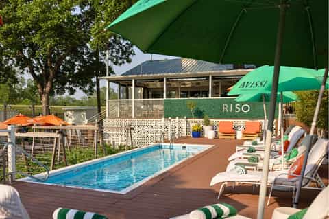 Rectangular resort pool with green umbrellas, loungers, and modern clubhouse with covered patio seating