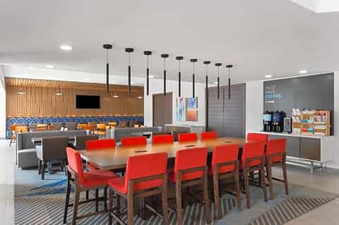 Modern hotel meeting room with red chairs, wooden accents, and glass-walled lounge areas