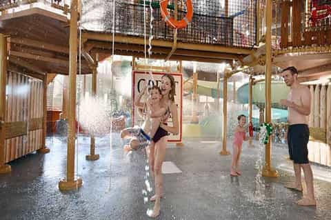 Indoor water park splash pad with families, wooden structures, water features, and safety netting