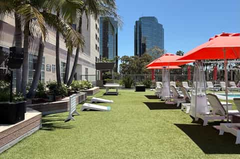 Outdoor lawn area with red umbrellas, white lounge chairs, palm trees, and modern hotel towers