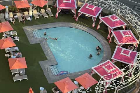Overhead view of curved pool with pink and coral umbrellas and lounge chairs