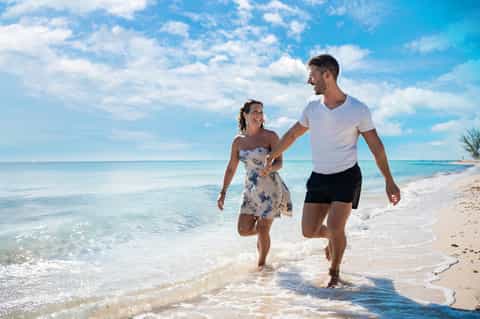 Couple running along pristine sandy beach with turquoise ocean water
