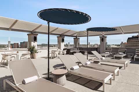 Modern rooftop terrace with lounge chairs, black umbrellas, pergola, and cityscape views in background