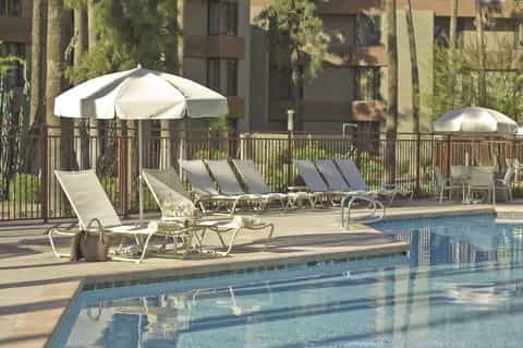 Resort pool area with lounge chairs, white umbrellas, palm trees, and residential building backdrop