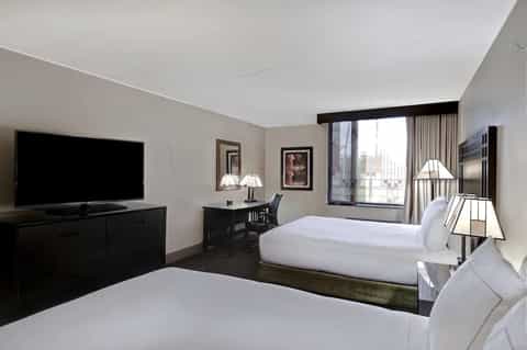 Hotel room with two beds, flat-screen TV, desk, and large window with city view