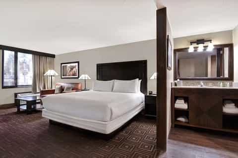 Modern hotel bedroom with king bed, dark wood furniture, and en-suite bathroom