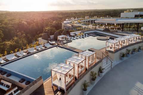 Aerial view of luxury resort pools, loungers, cabanas, and landscaping overlooking forest valley