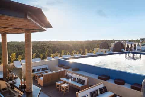 Rooftop infinity pool with lounge seating, wooden pergola, and panoramic forest and cityscape views