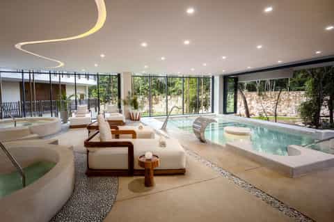 Luxurious indoor spa facility with multiple pools, lounge chairs, floor-to-ceiling windows, and natural light