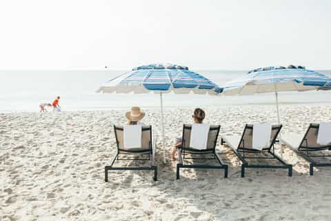 Beach lounge area with striped umbrellas, loungers, and ocean view with children playing