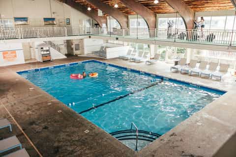 Indoor swimming pool with wooden arched ceiling, lounge chairs, and large windows with mountain views