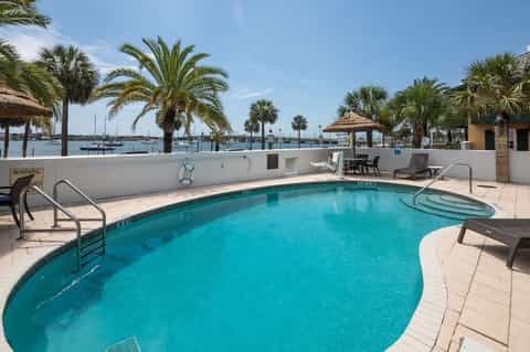 Waterfront pool with turquoise water, palm trees, boats, and tropical marina background
