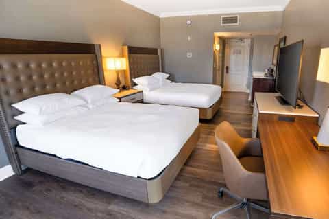 Modern hotel room with two queen beds, tufted headboards, and wooden desk area