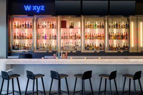 Upscale bar interior with illuminated bottle display and WXYZ neon sign above seating area