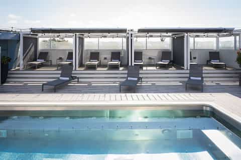 Modern rooftop pool area with loungers under retractable shade covers at sunset