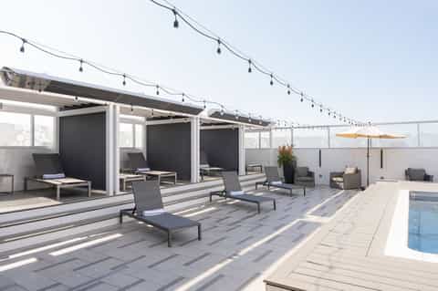 Hotel rooftop lounge with modern cabanas, string lights, lounge chairs, and pool area