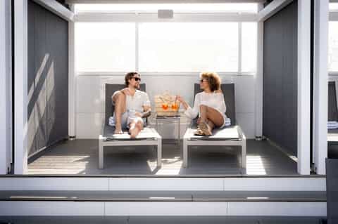 Two guests relaxing on a modern rooftop terrace with white lounge chairs and city views