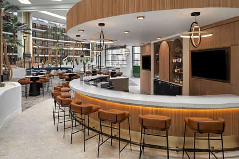 Modern hotel lobby bar with wood paneling, leather bar stools, and hanging pendant lights