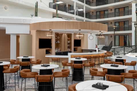 Contemporary hotel bar and lounge with wooden accents, tan leather chairs, and white tables